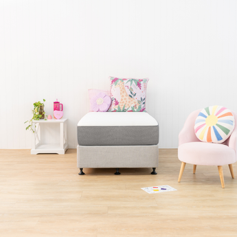 Children's room with a gray ottoman, pink chair, and colorful cushions on a wooden floor.