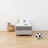 Bed with grey mattress cover and white box spring in a room with a soccer ball on the floor.