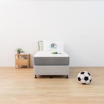 Bed with grey mattress cover and white box spring in a room with a soccer ball on the floor.