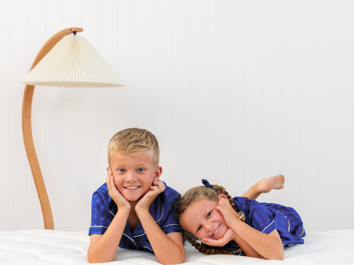 Two children in matching blue pajamas lying on a Naptime bed with a white background