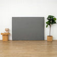 Grey foam headboard on a wooden floor with a plant and small table in the background