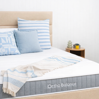 Bed with blue and white striped pillows, blanket, and Ortho Balance mattress.
