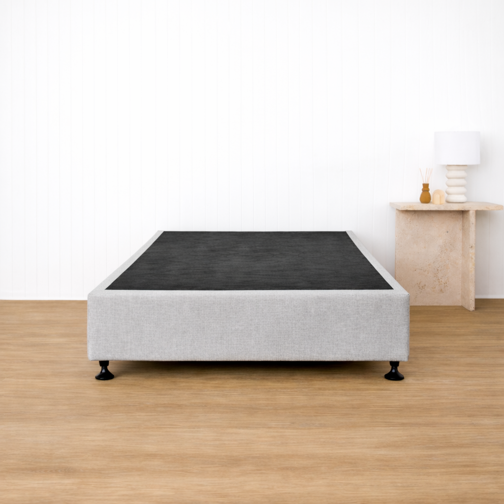 Naptime porto bed frame with black mattress on a wooden floor in a minimalistic room.