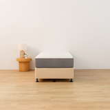Mattress on a wooden platform in a minimalistic room with a side table and plant.
