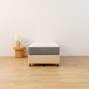 Mattress on a wooden platform in a minimalistic room with a side table and plant.