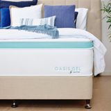 A mattress on a bed base with bedding and pillows, set in a room with wooden flooring, a window, and a plant.