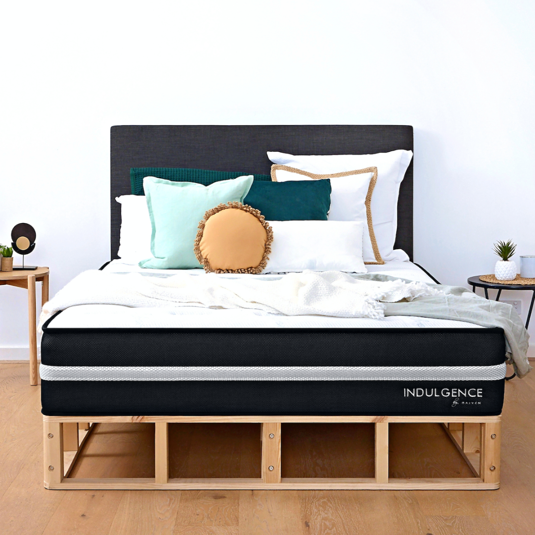 A Scandi Bed Base with a gray upholstered headboard, a white and gray mattress, and decorative pillows. The bed base has a simple wooden frame design.