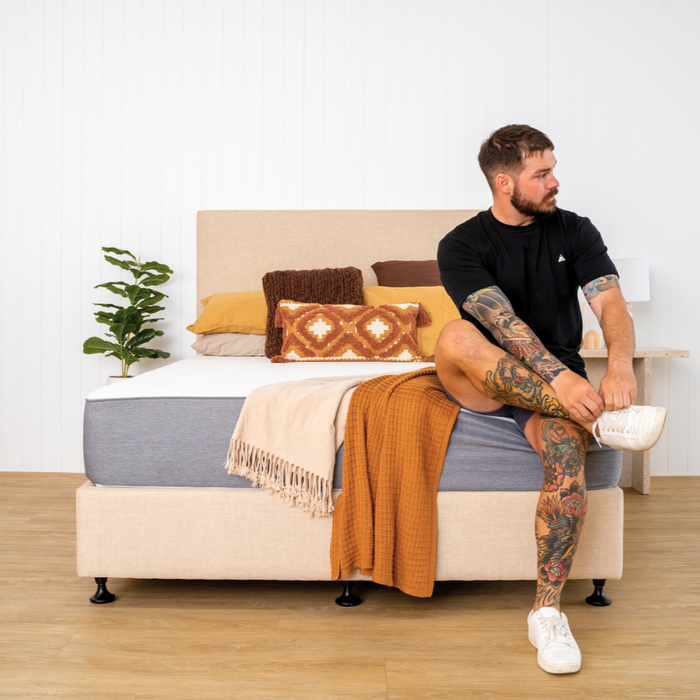 Bed base, mattress and a guy on side of mattress with pillows and throw
