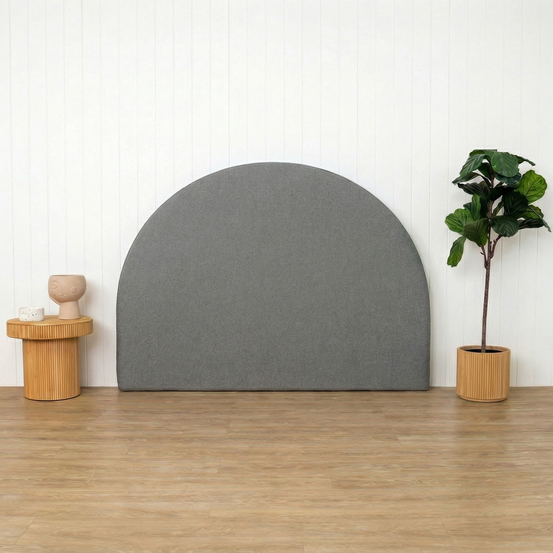 Grey arch-shaped headboard against a white wall with a wooden floor, small table, and plant.