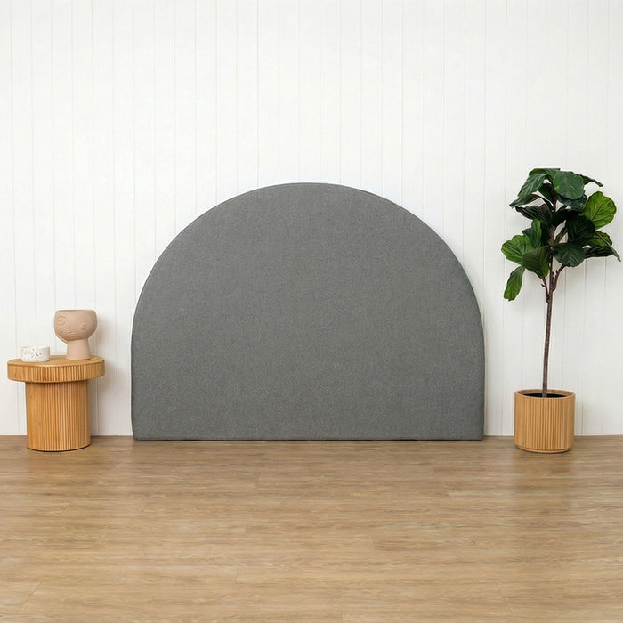 Grey arch-shaped headboard against a white wall with a wooden floor, small table, and plant.