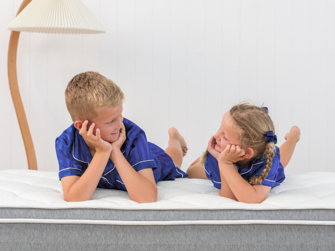 Two children in matching blue outfits lying on a Naptime mattress.