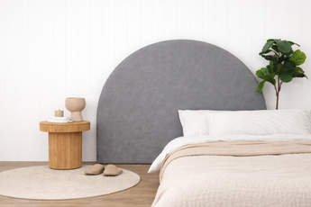Grey Luna foam headboard in a bedroom setting with a wooden side table and plant.