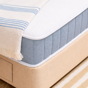 Ortho Balance mattress with a natural frame and white and blue striped blanket on top