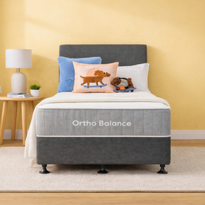 Ortho Balance mattress and base with decorative pillows in a room with a yellow wall and wooden floor.
